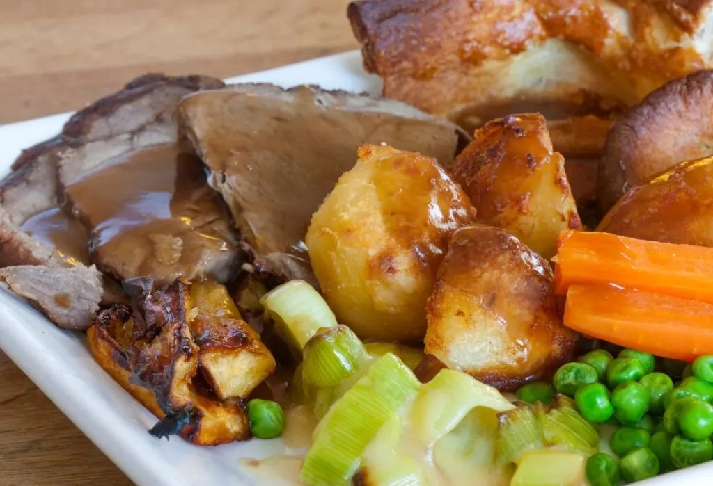 roasted potatoes served alongside roast beef, Yorkshire pudding and vegetables with gravy poured over the top.