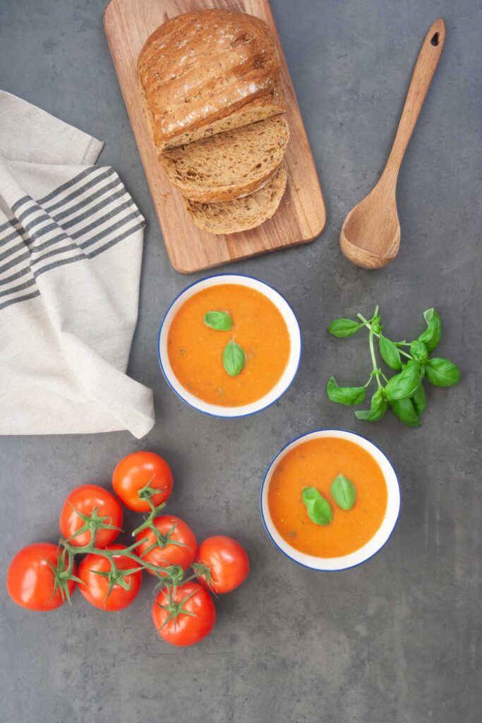 tomato and basil soup with fresh tomatoes and basil next to a loaf of bread