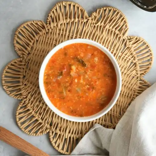 vegetable and lentil soup in a bowl on a placemat with a wooden spoon and cloth next to the ninja soup maker and blender