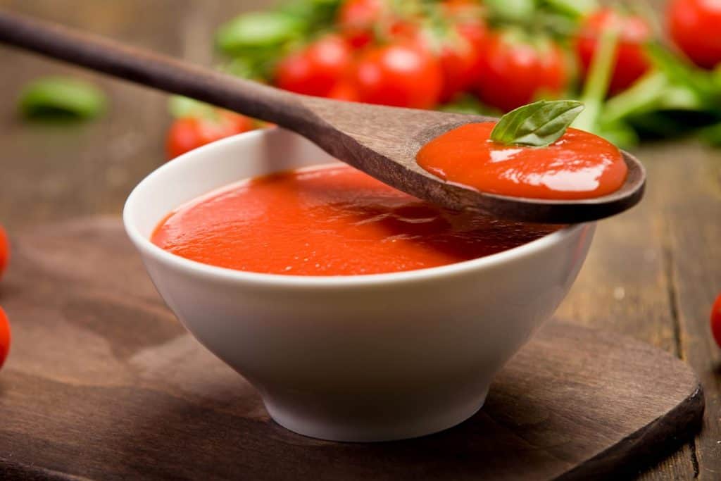 tomato passata in a bowl with a wooden spoon on top with herbs