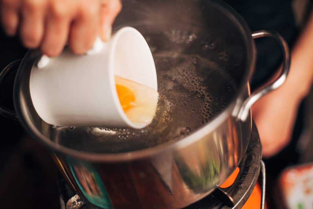 adding egg to boiling water from a mug for poached egg