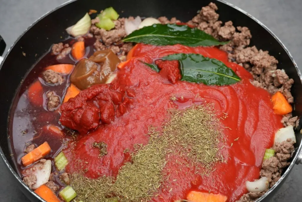 adding passata, puree, bay leaves, herbs, beef stock and red wine to beef mince for lasagne