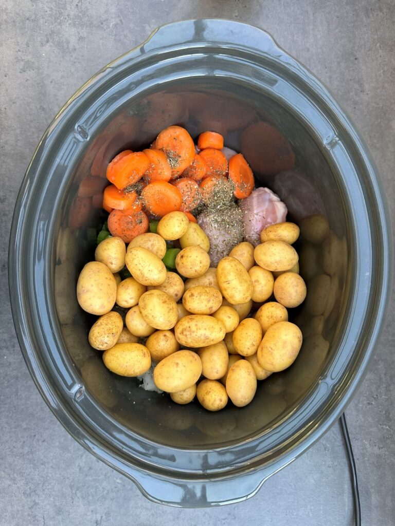 new potatoes added to slow cooker with carrots, herbs, celery and raw chicken