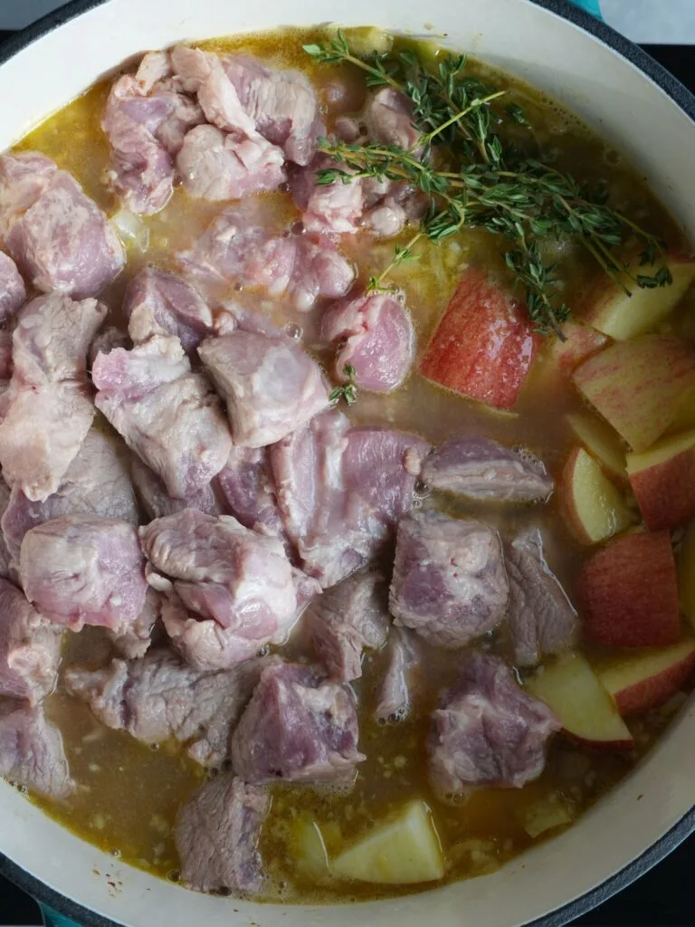 pork and apple in casserole dish with thyme cider and stock