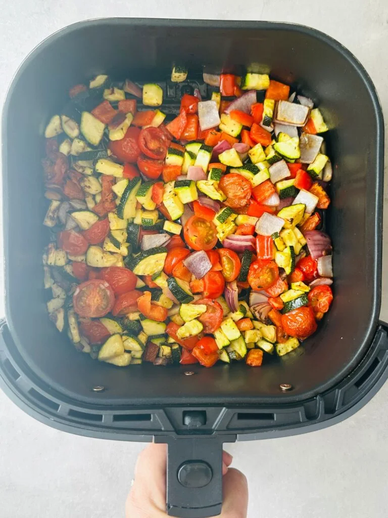 chopped vegetables (courgette, red pepper, cherry tomatoes and red onion) in an air fryer basket