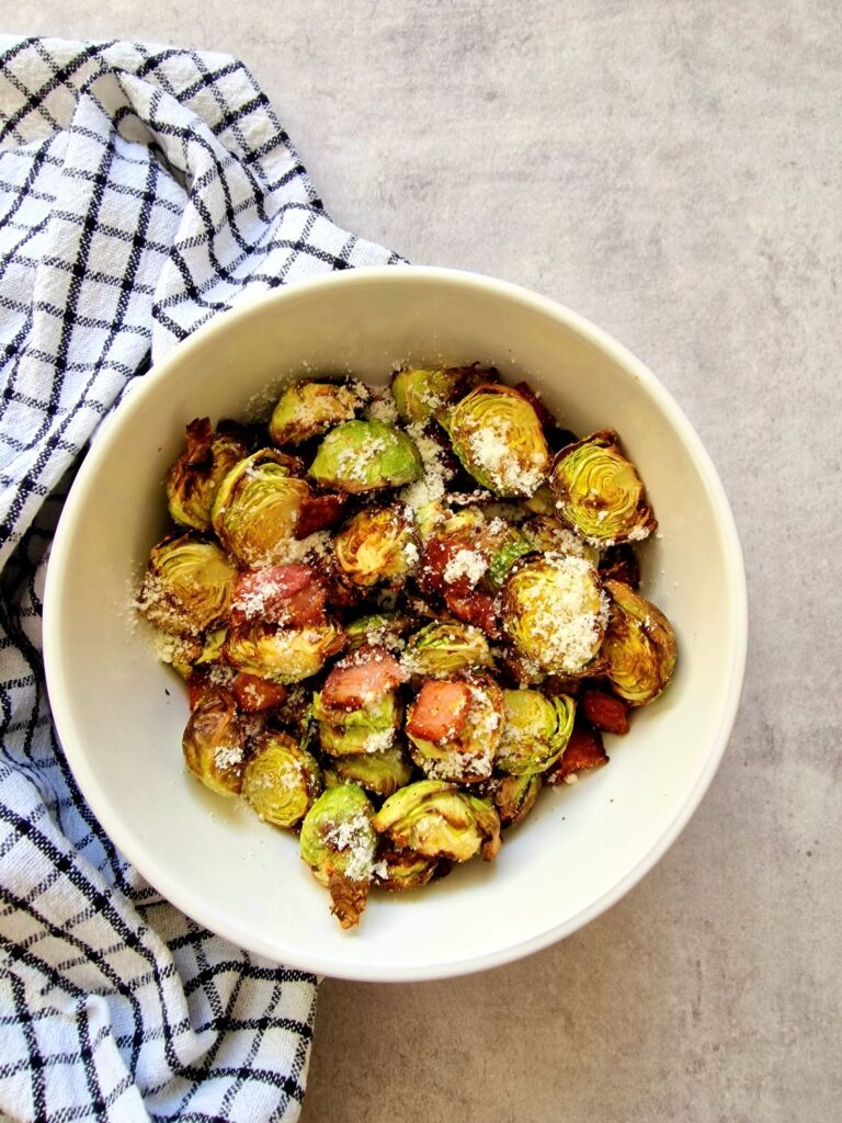 brussel sprouts and bacon in a white bowl next to a black and white teatowel