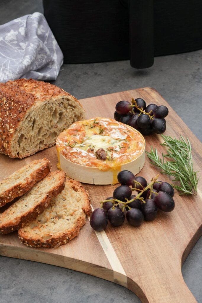 melted camembert cooked in an air fryer next to sliced bread, grapes and fresh rosemary 