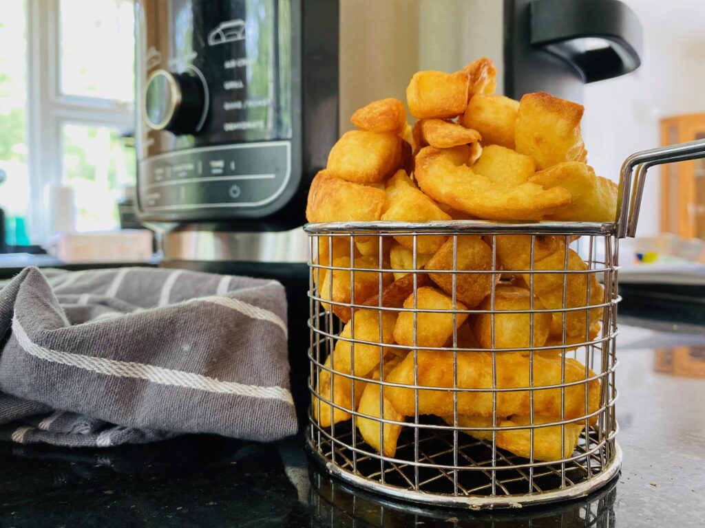 frozen chips cooked in the air fryer and placed in a wire serving basket next to the Ninja Foodi