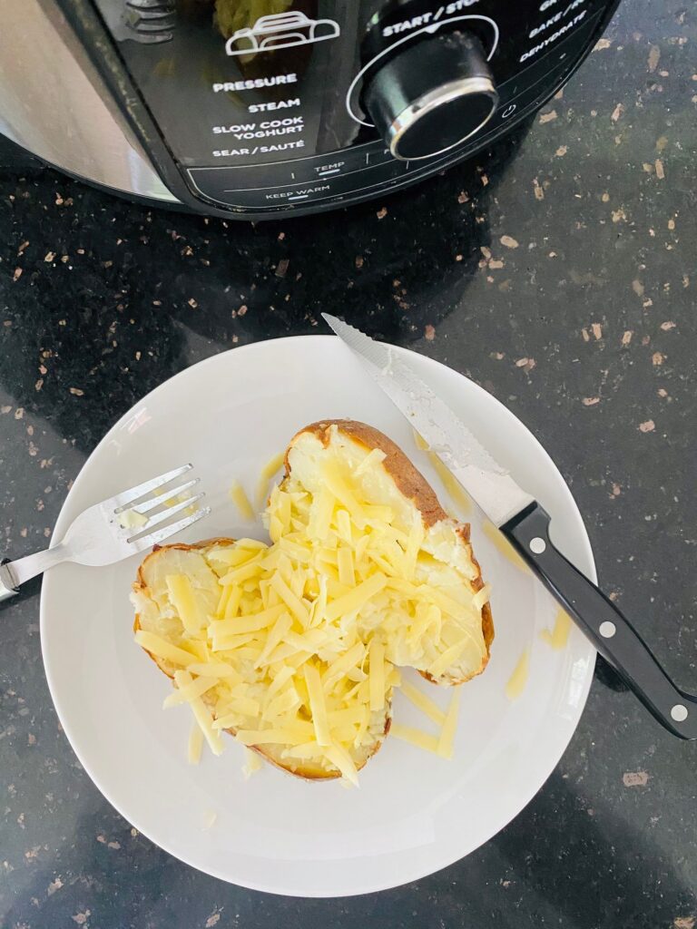 grated cheese on an air fryer jacket potato on a plate next to Ninja Foodi Max Air Fryer