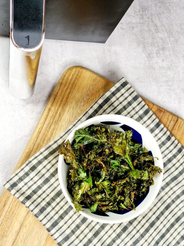 crispy kale chips in a bowl next to a Ninja air fryer