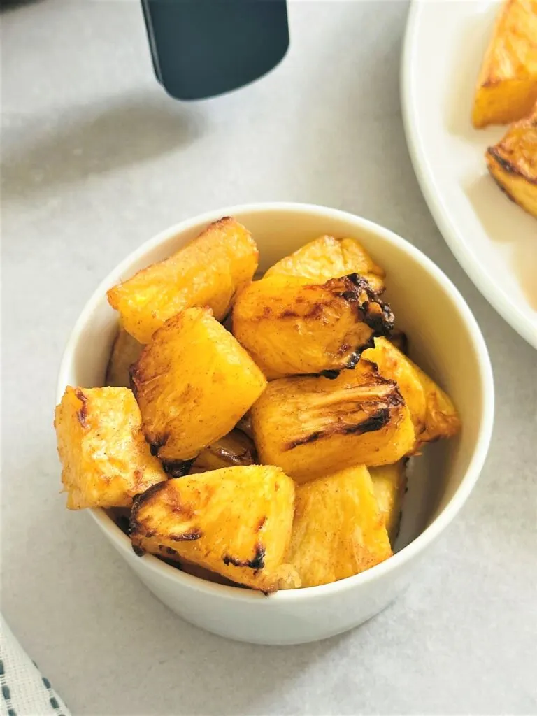 air fried pineapple chunks in a bowl next to an air fryer