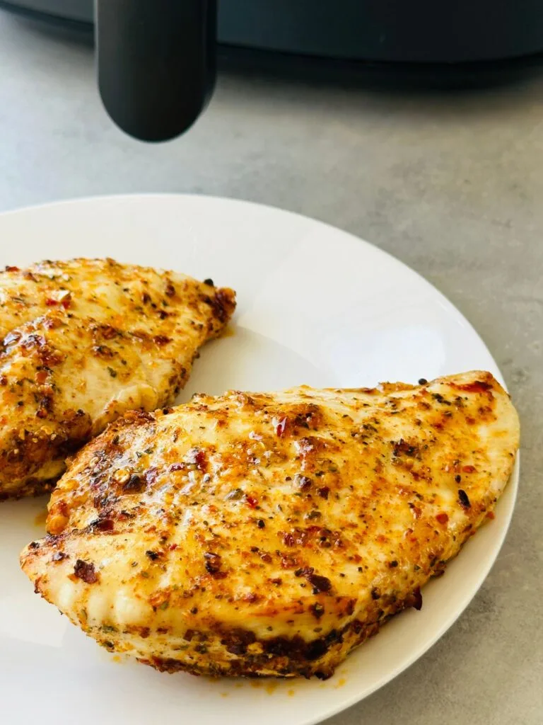 two piri piri chicken breasts on a white plate next to an air fryer