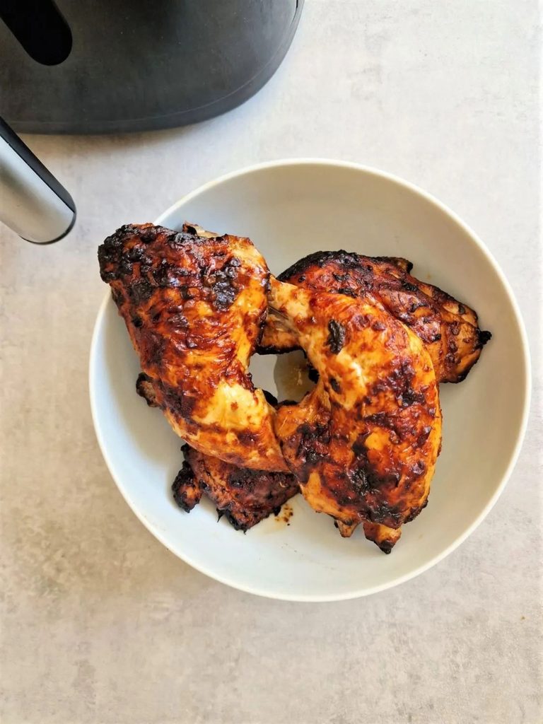 piri piri chicken legs in a bowl next to an air fryer