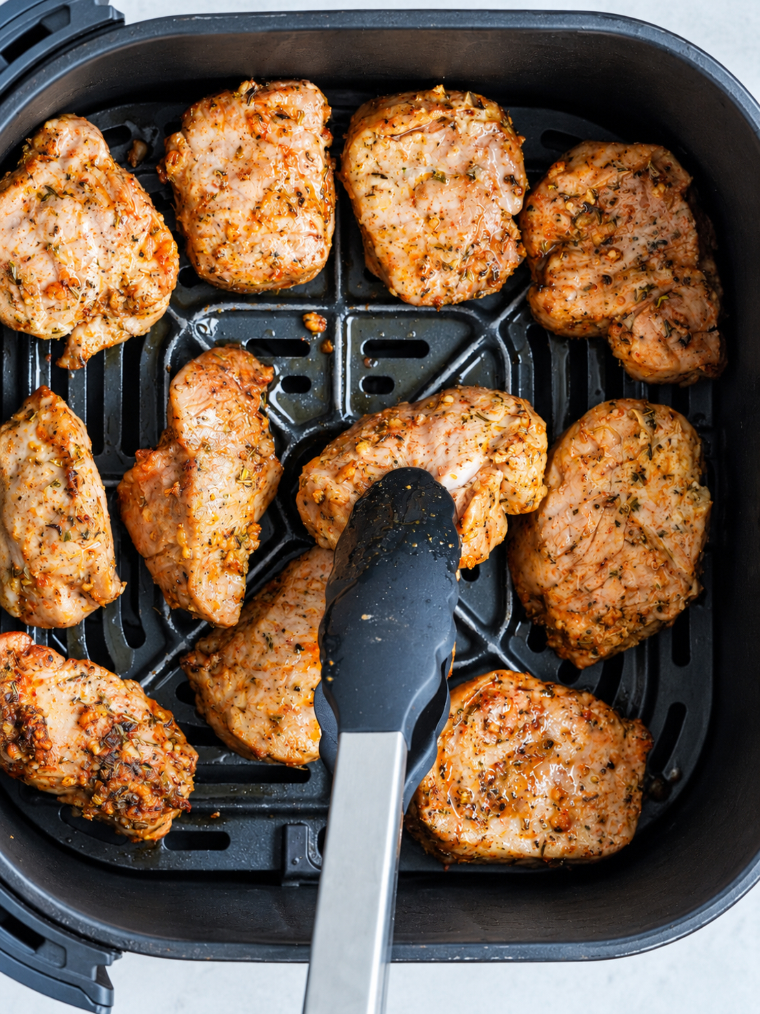 pork medallions in the air fryer with tongs picking one up