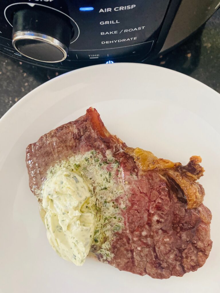 air fryer steak next to Ninja Foodi with garlic and herb butter on top