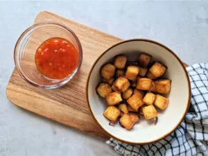air fried tofu in a bowl next to sweet chilli sauce in a ramekin dish