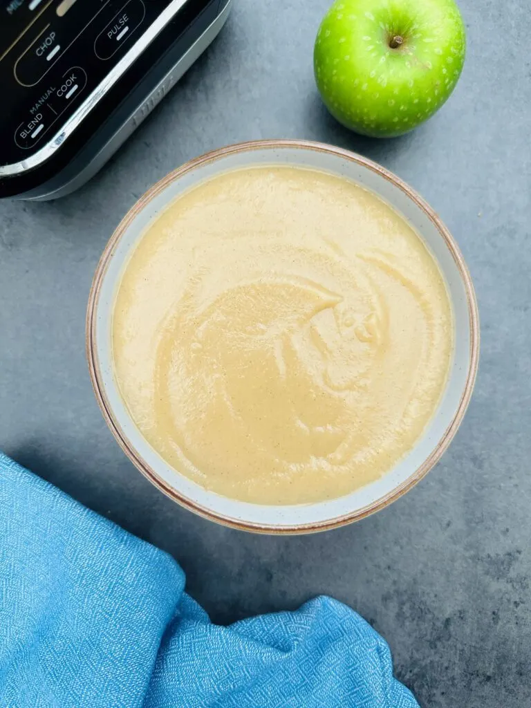 apple and parsnip soup in a bowl next to a soup maker and a Granny Smith apple