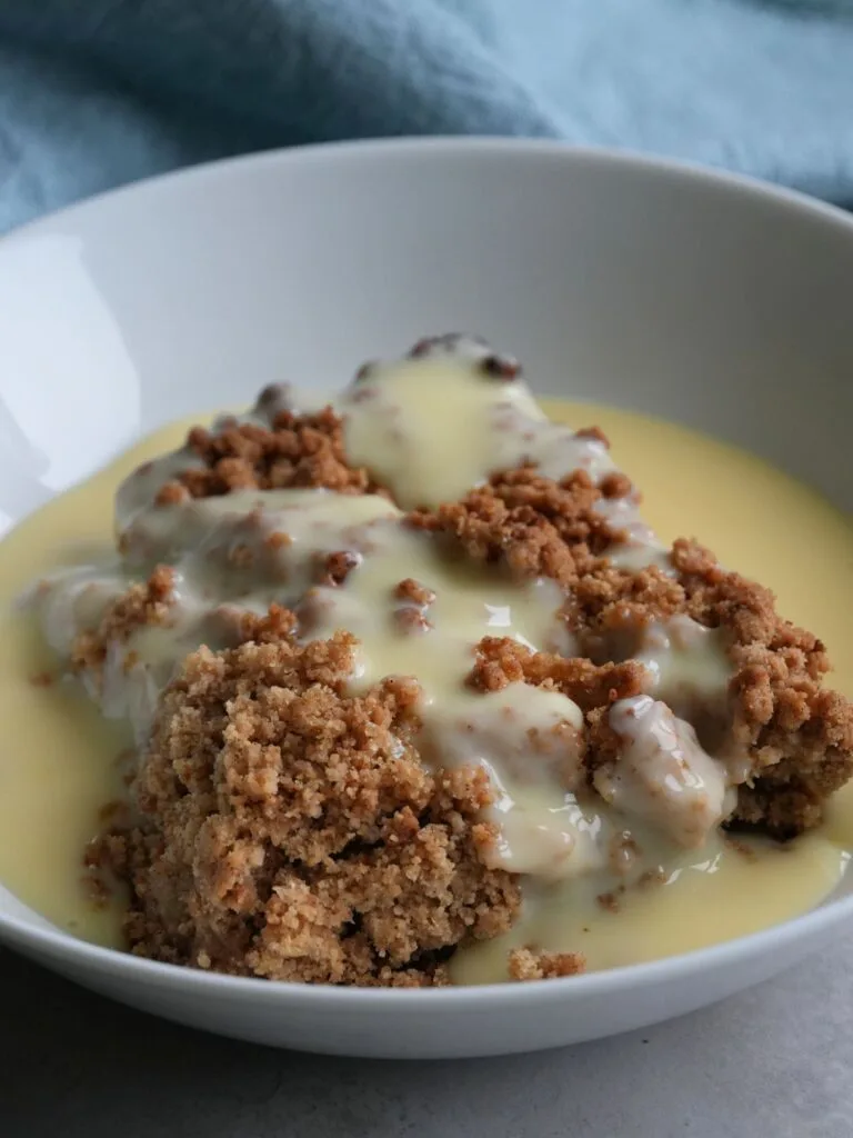 apple crumble in bowl with fresh custard on top 