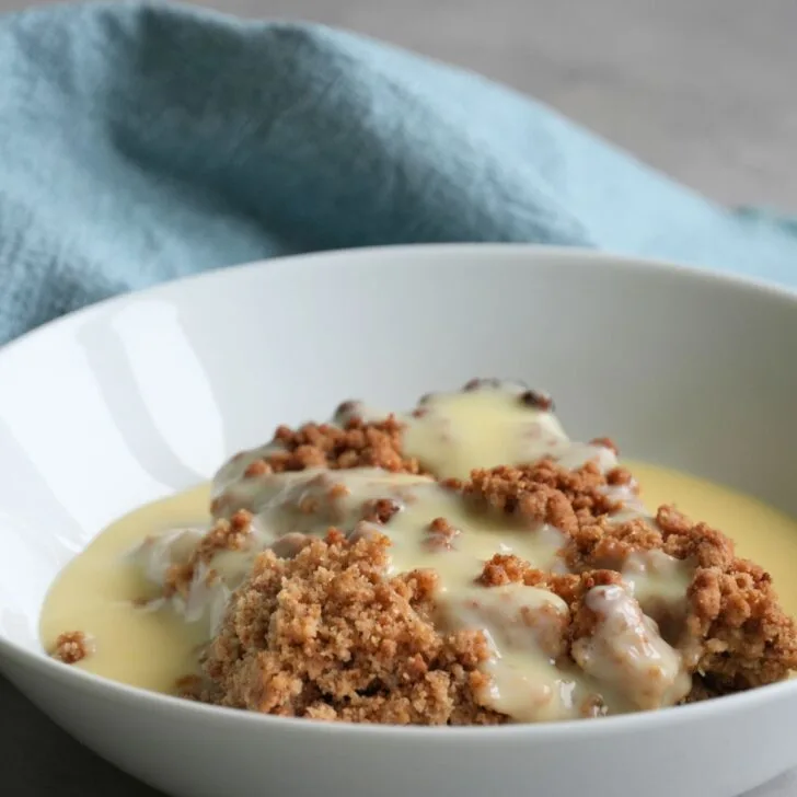 apple crumble in bowl with fresh custard on top