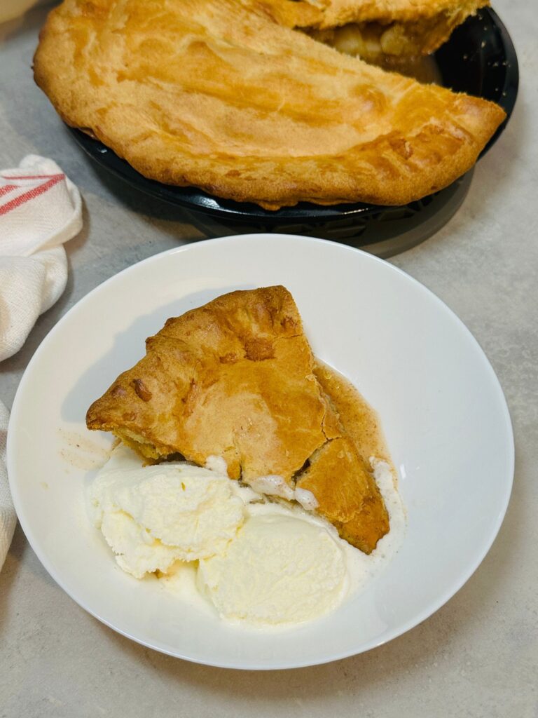 slice of apple pie with ice cream in front of the rest of the apple pie