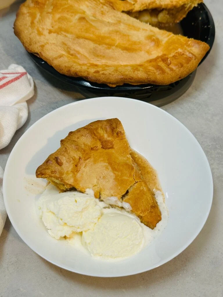 slice of apple pie with ice cream in front of the rest of the apple pie