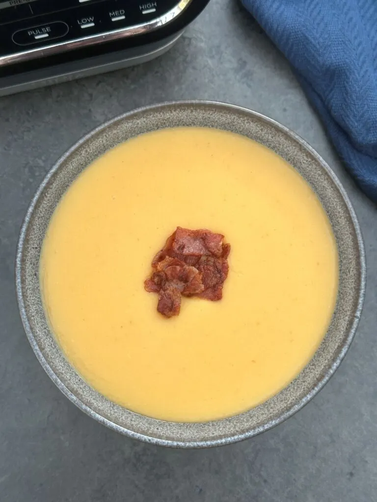 bacon and lentil soup in a grey bowl next to a Ninja soup maker