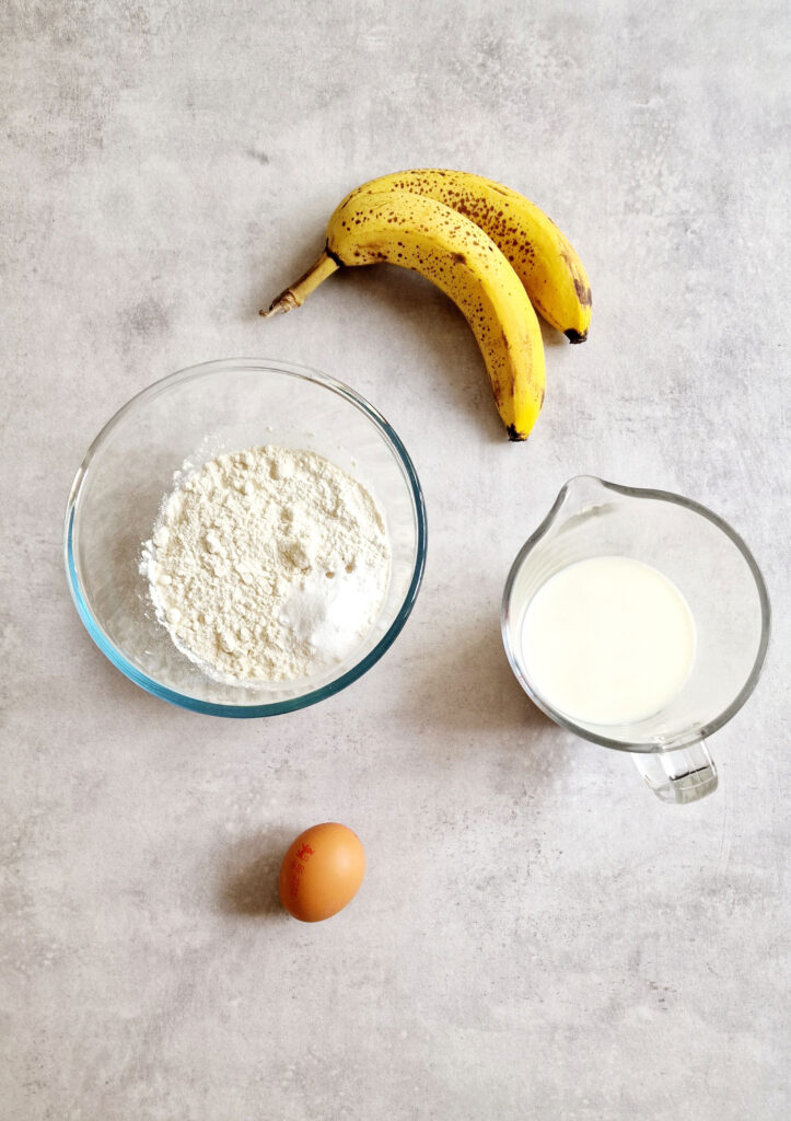ingredients laid out for banana pancakes - 2 ripe bananas, flour and salt, milk and an egg