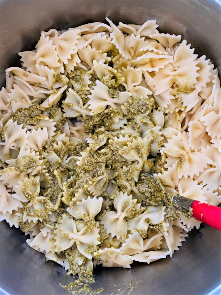 stirring basil pesto into cooked pasta