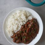 beef and ale stew next to rice on a plate with part of a casserole dish showing at the edge