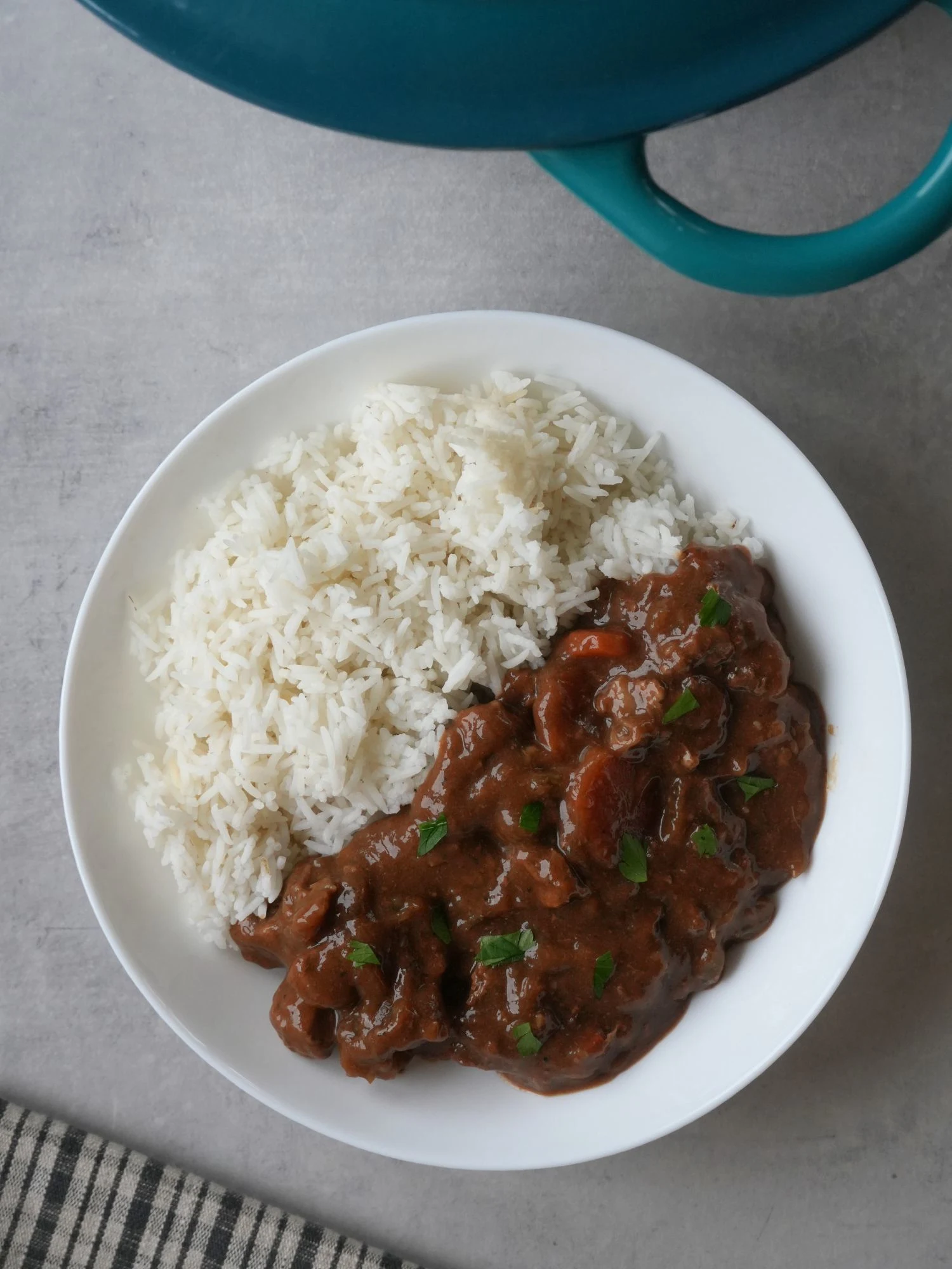 beef and ale stew next to rice on a plate with part of a casserole dish showing at the edge