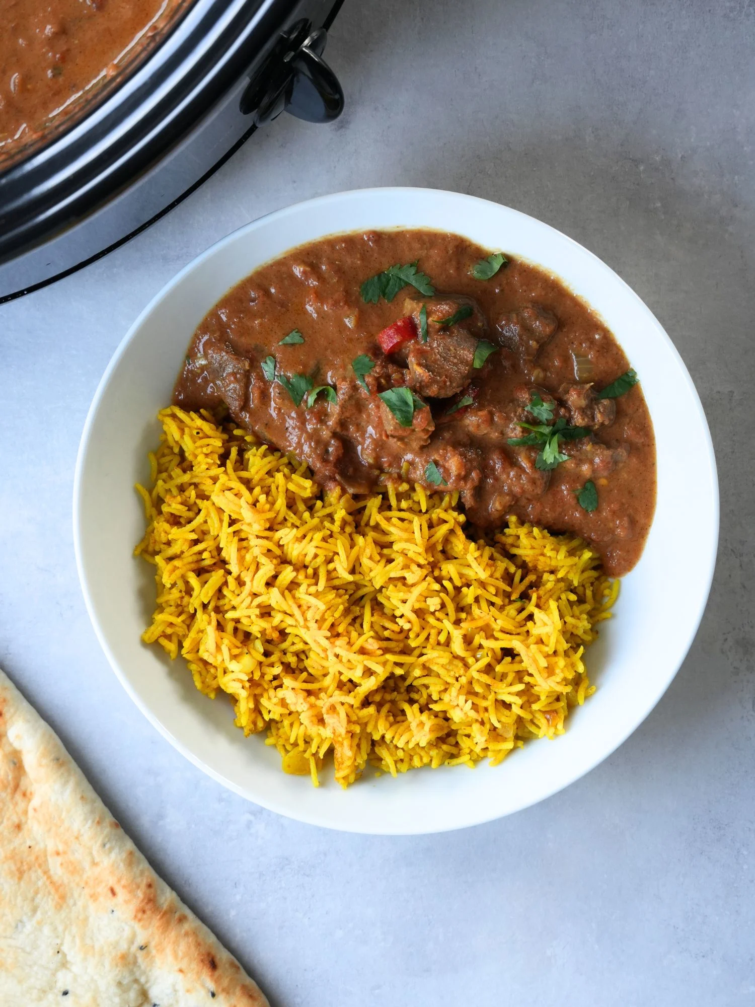 beef curry next to pilau rice and naan bread and slow cooker