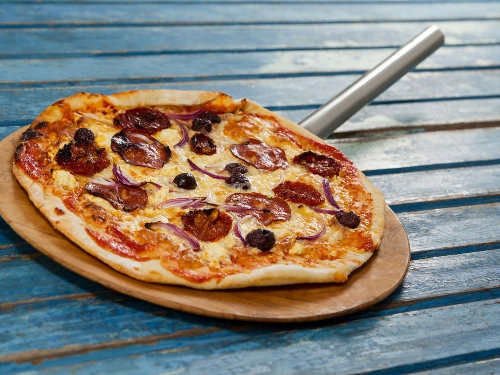 cooked pizza with pepperoni on pizza peel after being cooked in a gas pizza oven