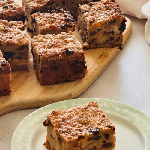 slice of bread pudding on a plate in front of a chopping board of other sliced bread pudding