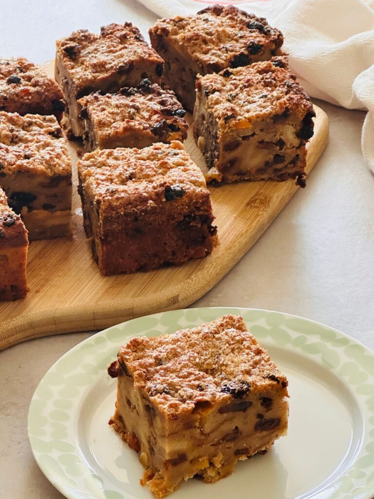slice of bread pudding on a plate in front of a chopping board of other sliced bread pudding