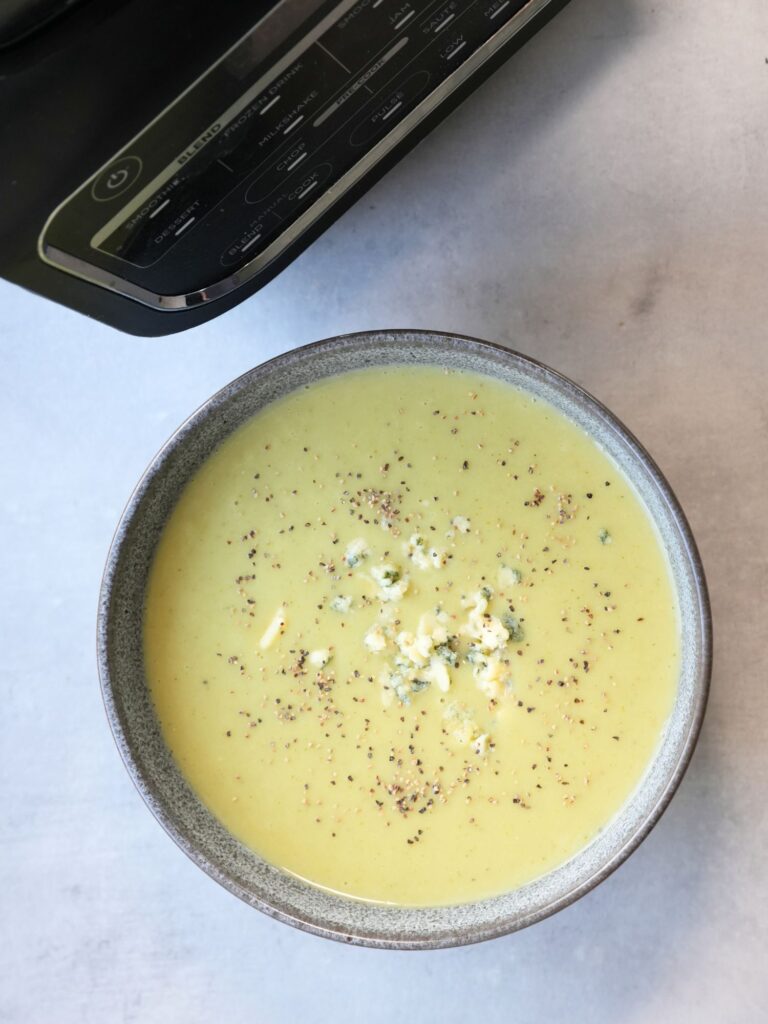 broccoli and stilton soup in a bowl with crumbled stilton on top next to a ninja soup maker