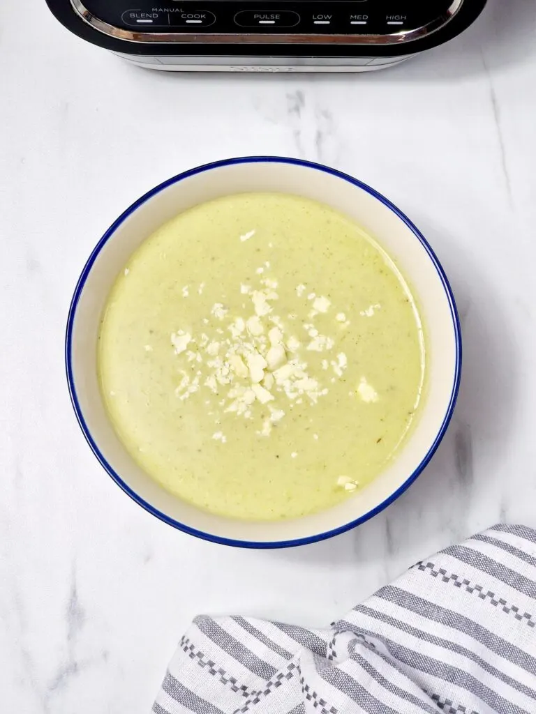 Broccoli coconut and ginger soup with crumbled cheese on top next to Ninja Soup Maker