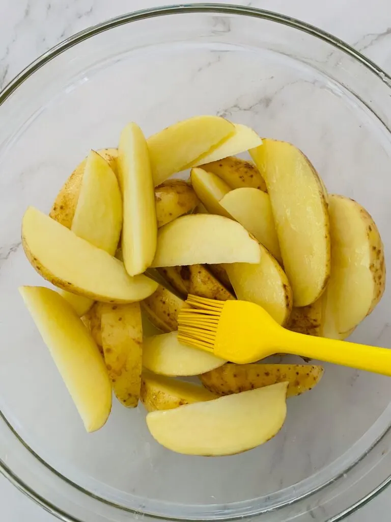 oiling potato wedges with a brush before adding them to the Ninja Foodi Air Fryer