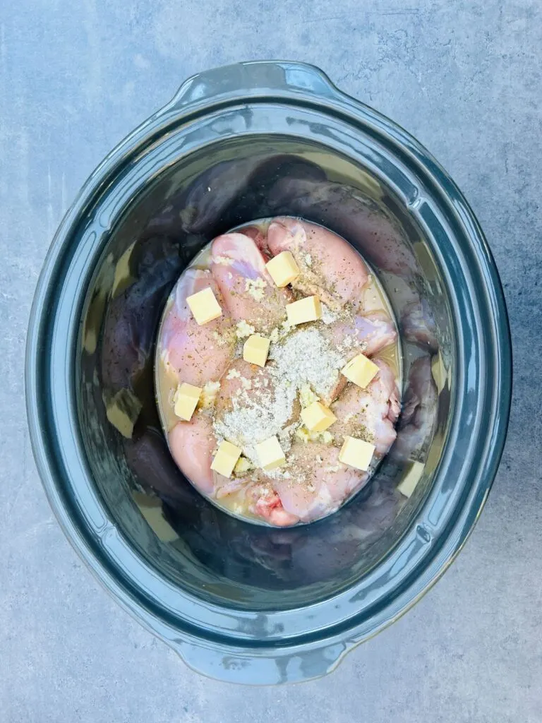 butter and seasonings on chicken in slow cooker