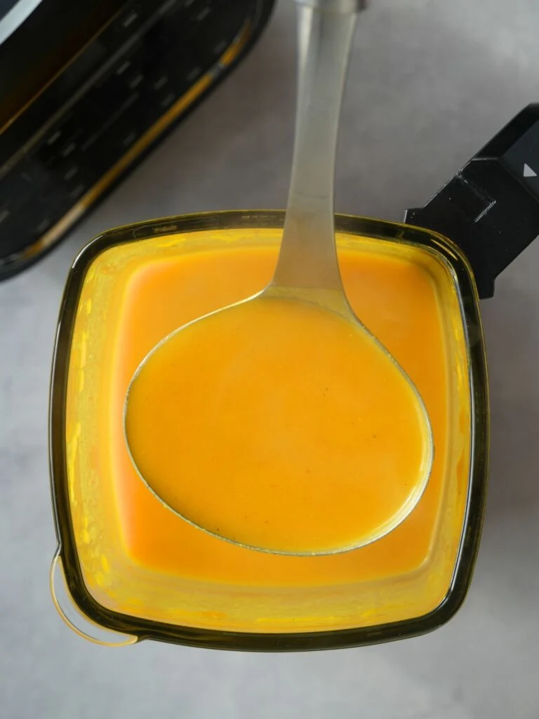 overhead view of cooked butternut squash soup with a soup ladle holding some of the soup above a Ninja soup maker