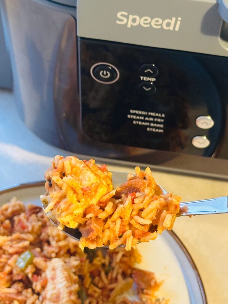 close up of cajun chicken and rice on a spoon above a plate with it on and in front of the Ninja Speedi