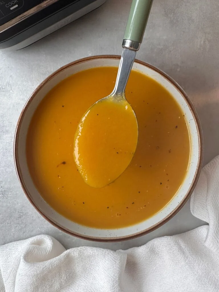 carrot and celery soup in a bowl with a spoon held above it with part of a ninja soup maker in the corner