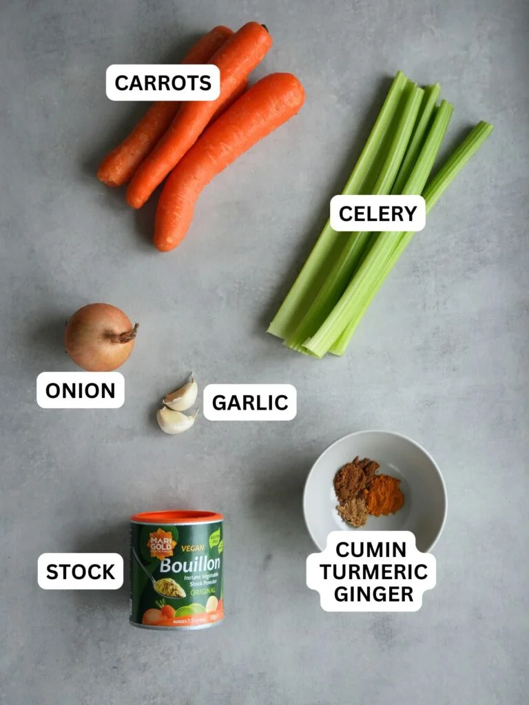 ingredients laid out and labelled for making carrot and celery soup in a soup maker: carrots, celery, onion, garlic, stock, cumin, turmeric and ginger