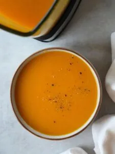 carrot and celery soup in a bowl with ground black pepper sprinkled on top next to part of a ninja soup maker