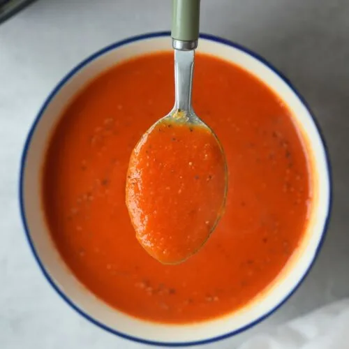 tomato and carrot soup in a bowl with a spoonful of the soup help above it.