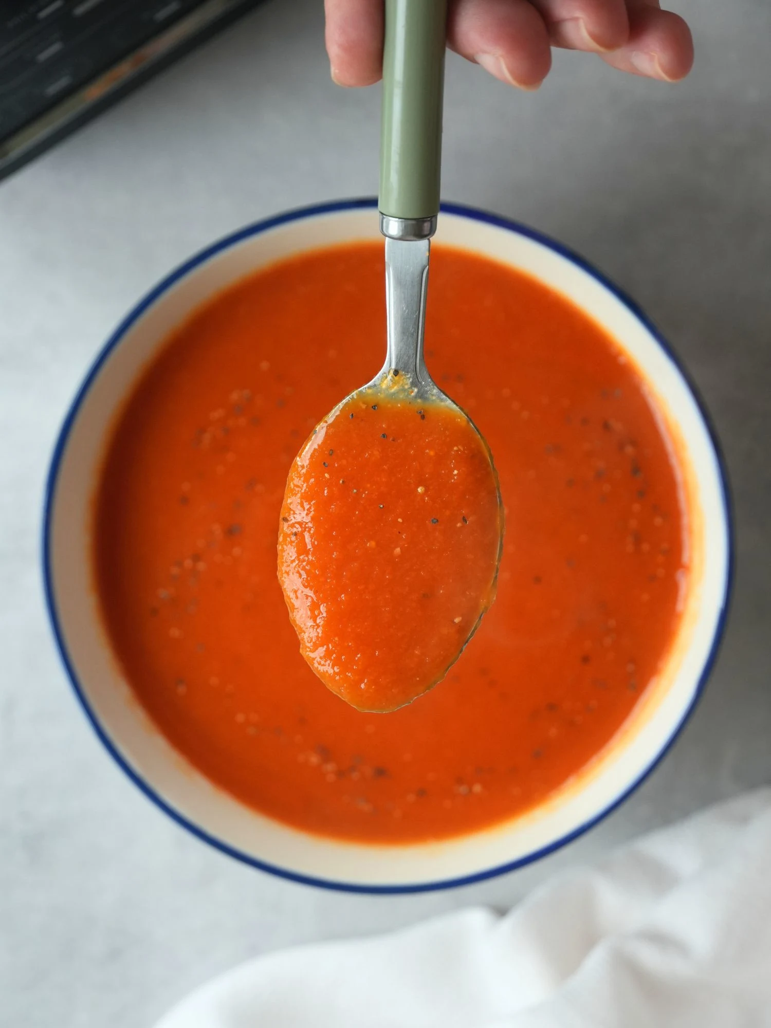 tomato and carrot soup in a bowl with a spoonful of the soup help above it.