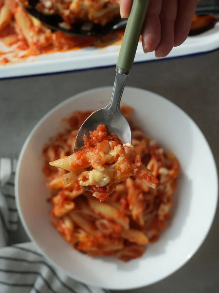 cheesy chicken pasta bake on a spoon above a white bowl