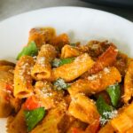 chicken and chorizo pasta on a plate with fresh basil leaves and grated parmesan cheese