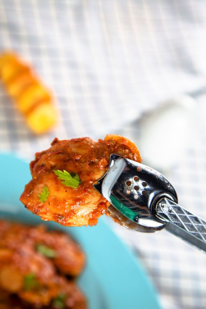 chunk of salsa chicken held with some serving tongs above a plate of slow cooker chicken salsa. 