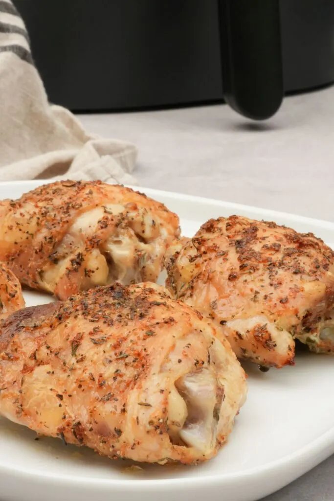four chicken thighs on a plate next to an air fryer