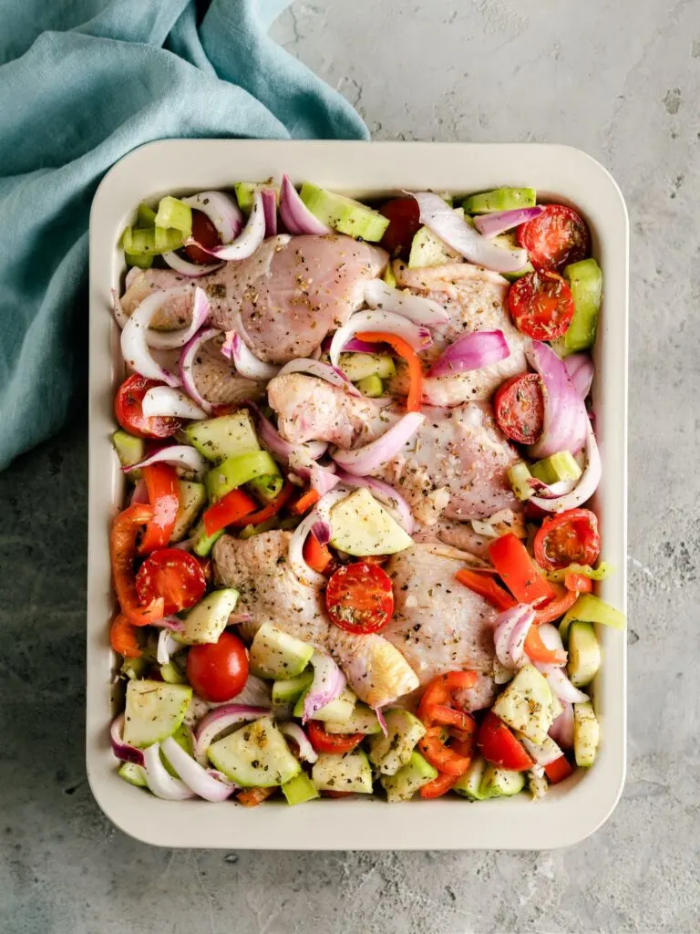 raw chicken mixed with potatoes, vegetables for roasting to make a Mediterranean chicken thigh tray bake